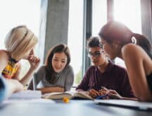 Group of young people sitting at table reading books.