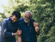 A man and his elderly father walking in a garden on a summer day.